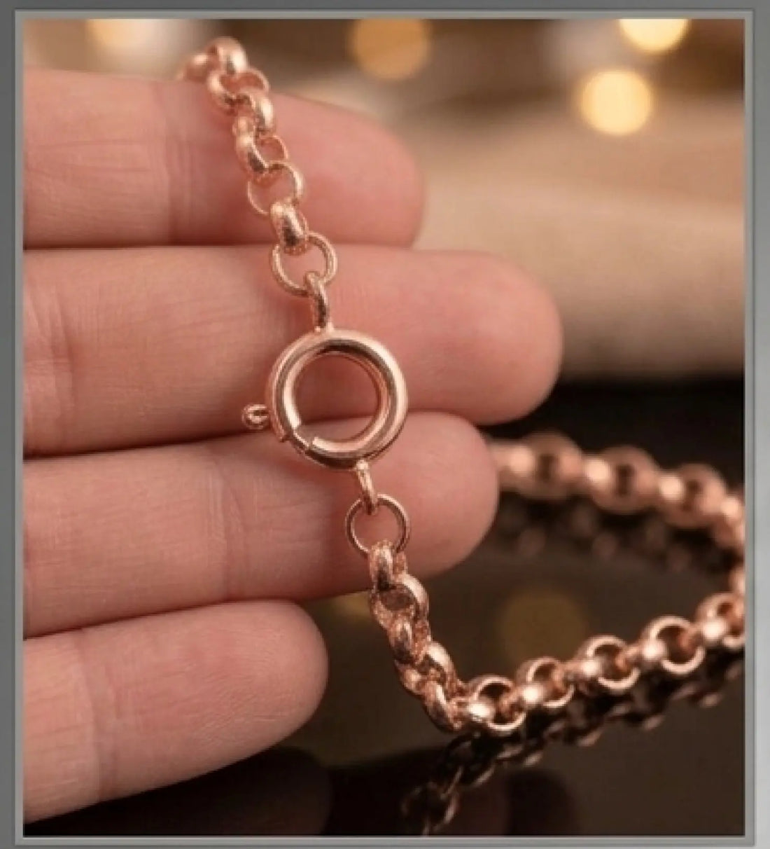 Rose gold chain with clasp held between fingers against a blurred background