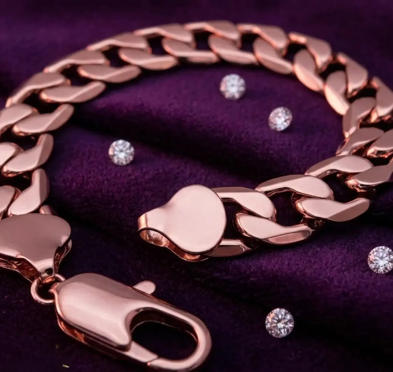 Rose gold chain bracelet with diamond earrings on a purple fabric background