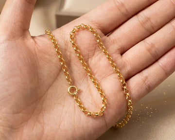 Gold chain held in a hand against a neutral background