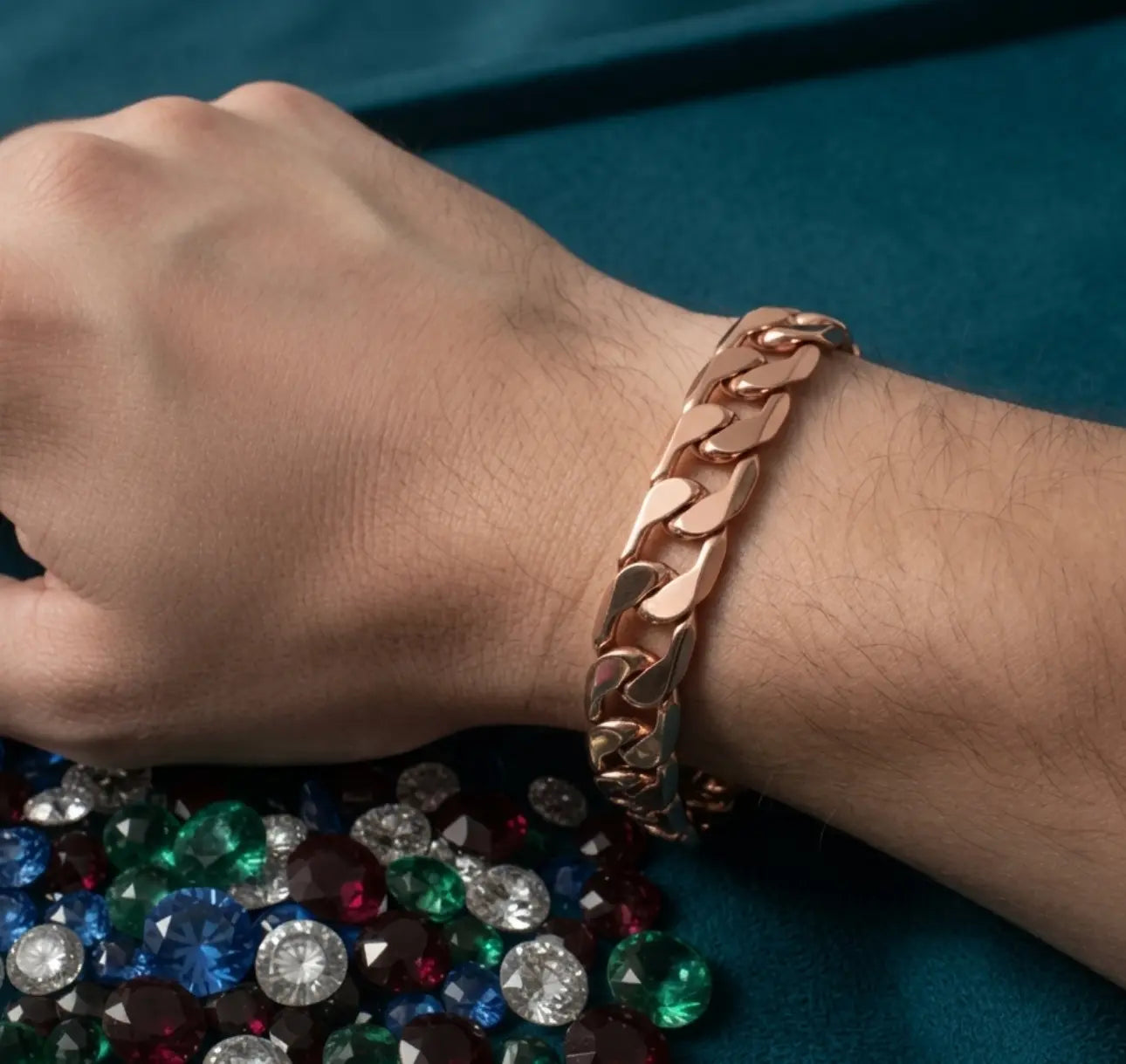 Rose gold chain bracelet on a wrist with colorful gemstones below