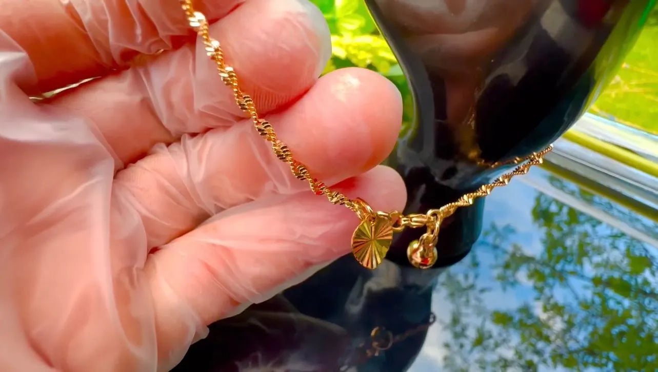 Gold necklace with a pendant held by a gloved hand against a blurred outdoor background.