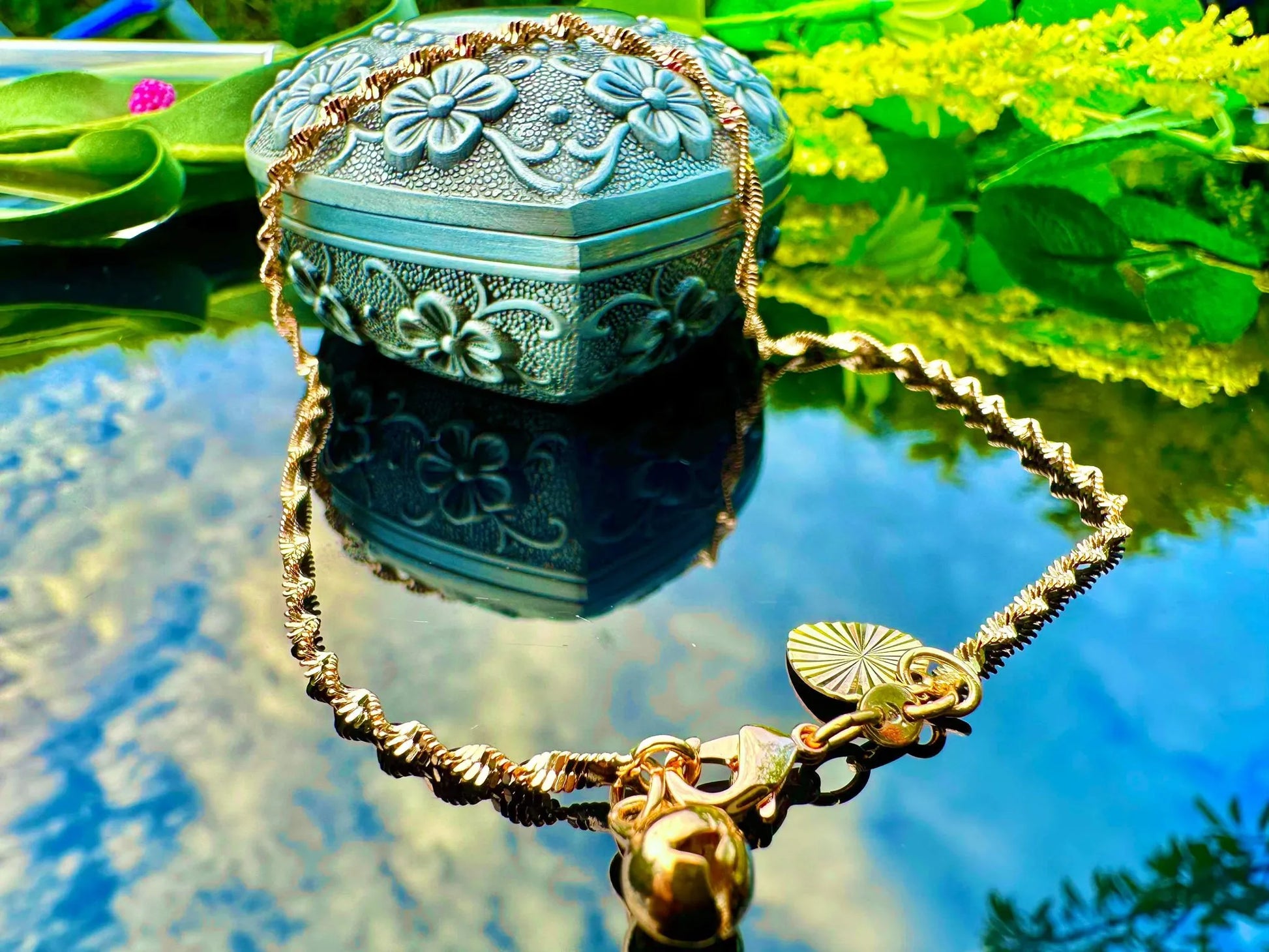 Decorative jewelry box with floral designs on a reflective surface surrounded by greenery