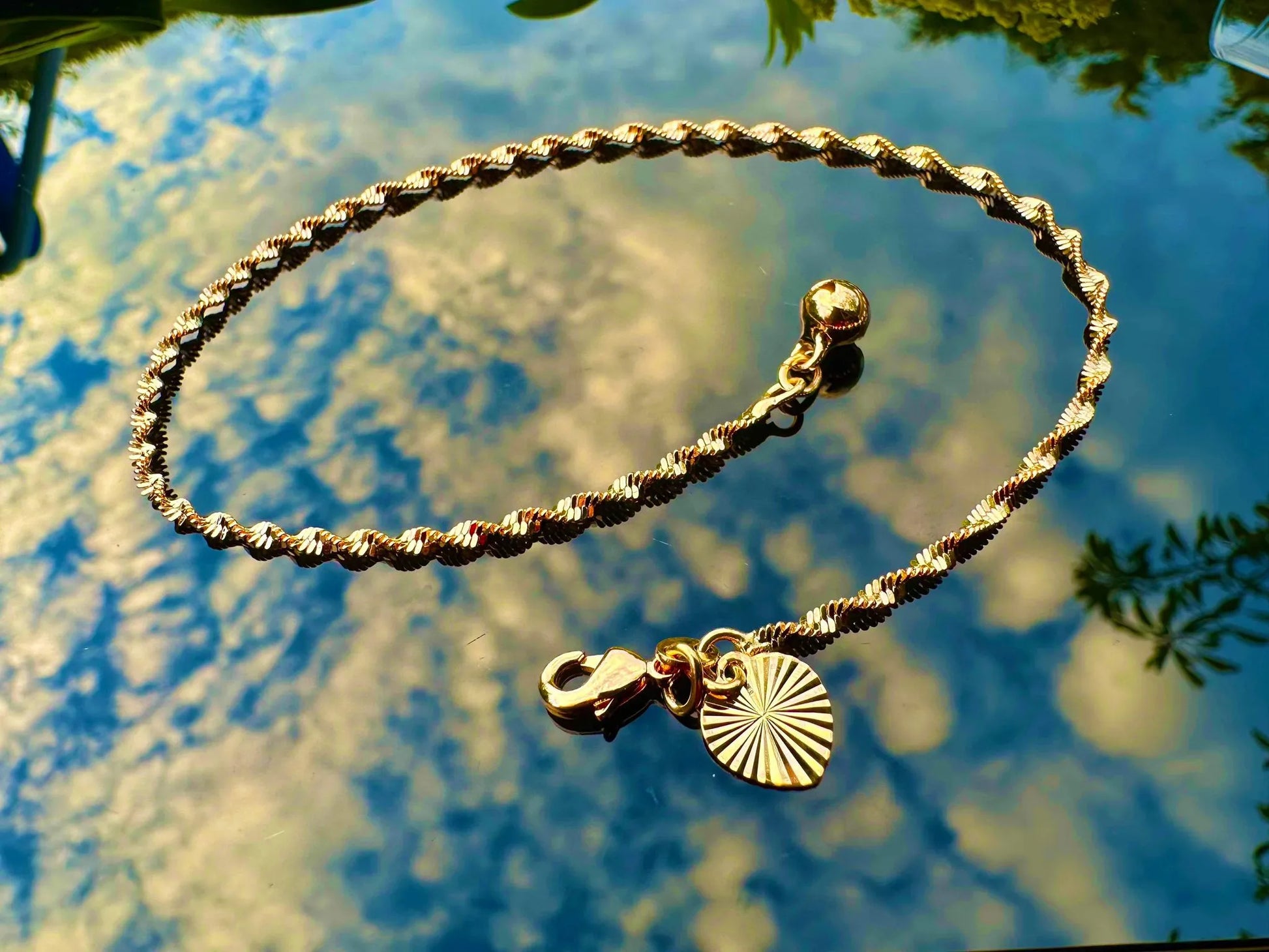 Gold bracelet with charms on a reflective water surface