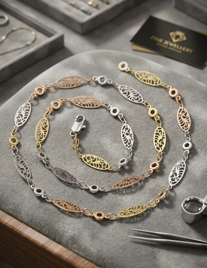 Gold, silver, and rose gold necklace on a gray surface with jewelry tools and a box in the background.