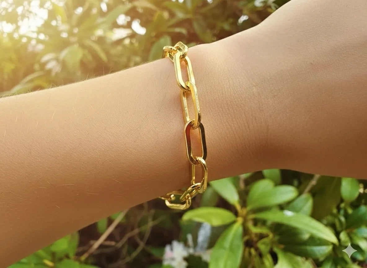 Gold chain bracelet on a wrist with a blurred green background