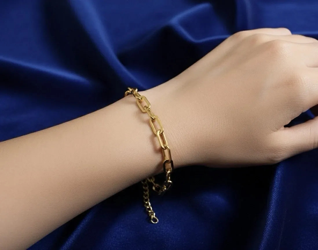 Gold chain bracelet on a wrist against a blue satin background