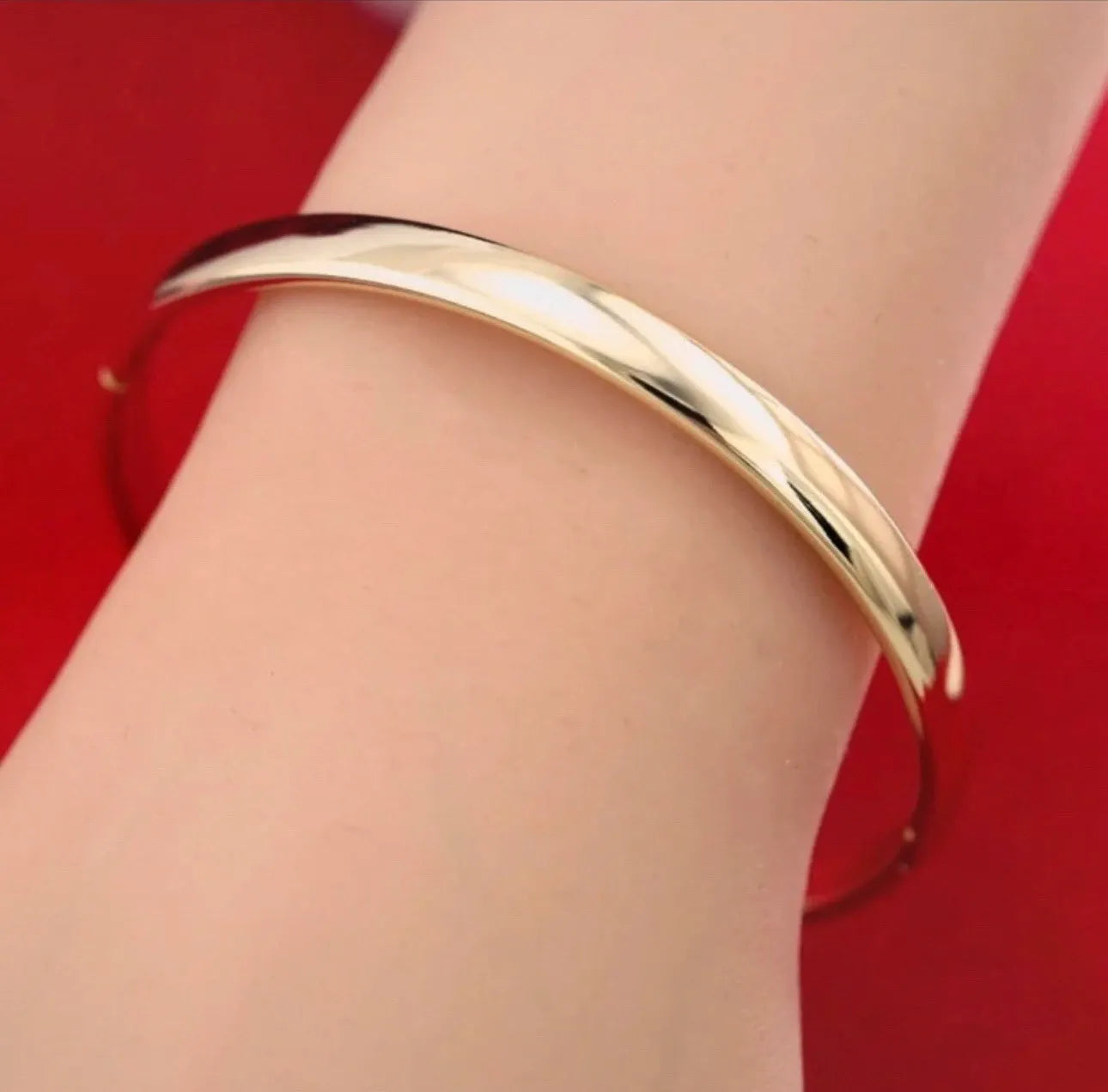 Gold bracelet on a wrist against a red background