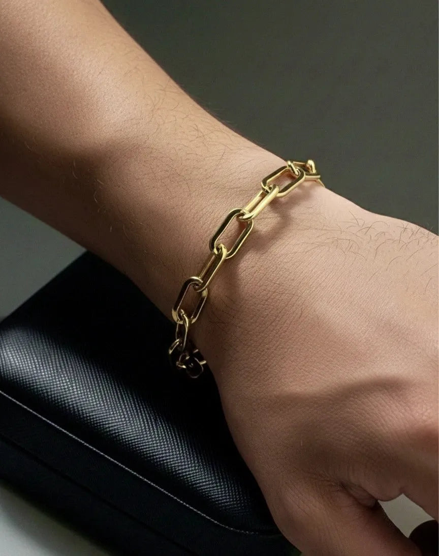 Gold chain bracelet on a wrist with a dark background