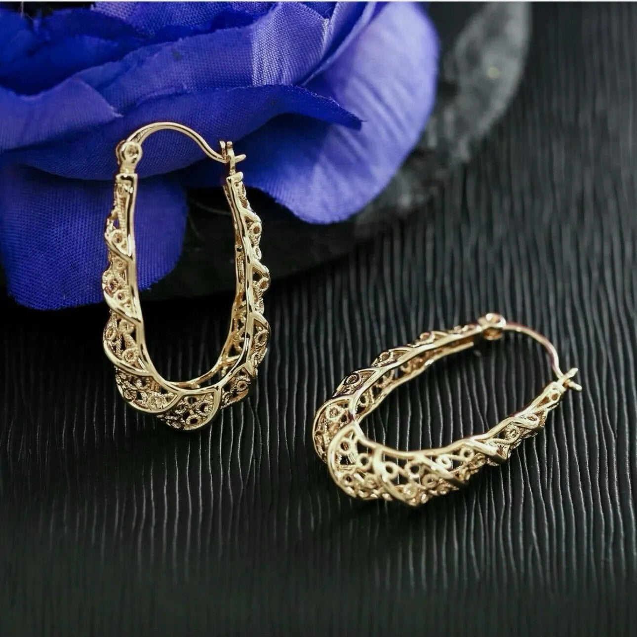 Gold hoop earrings on a dark surface with a blue flower in the background