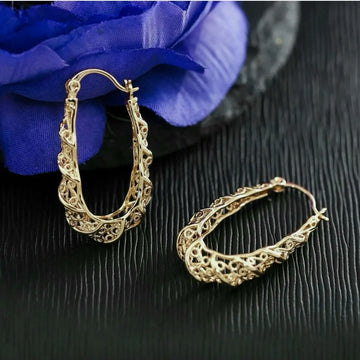 Gold hoop earrings on a dark surface with a blue flower in the background