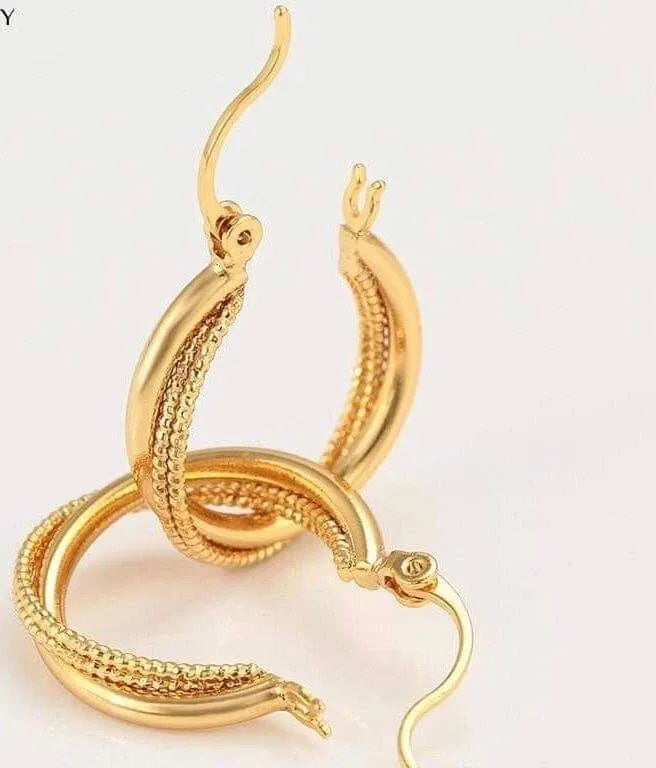 Gold snake-shaped earrings on a light pink background
