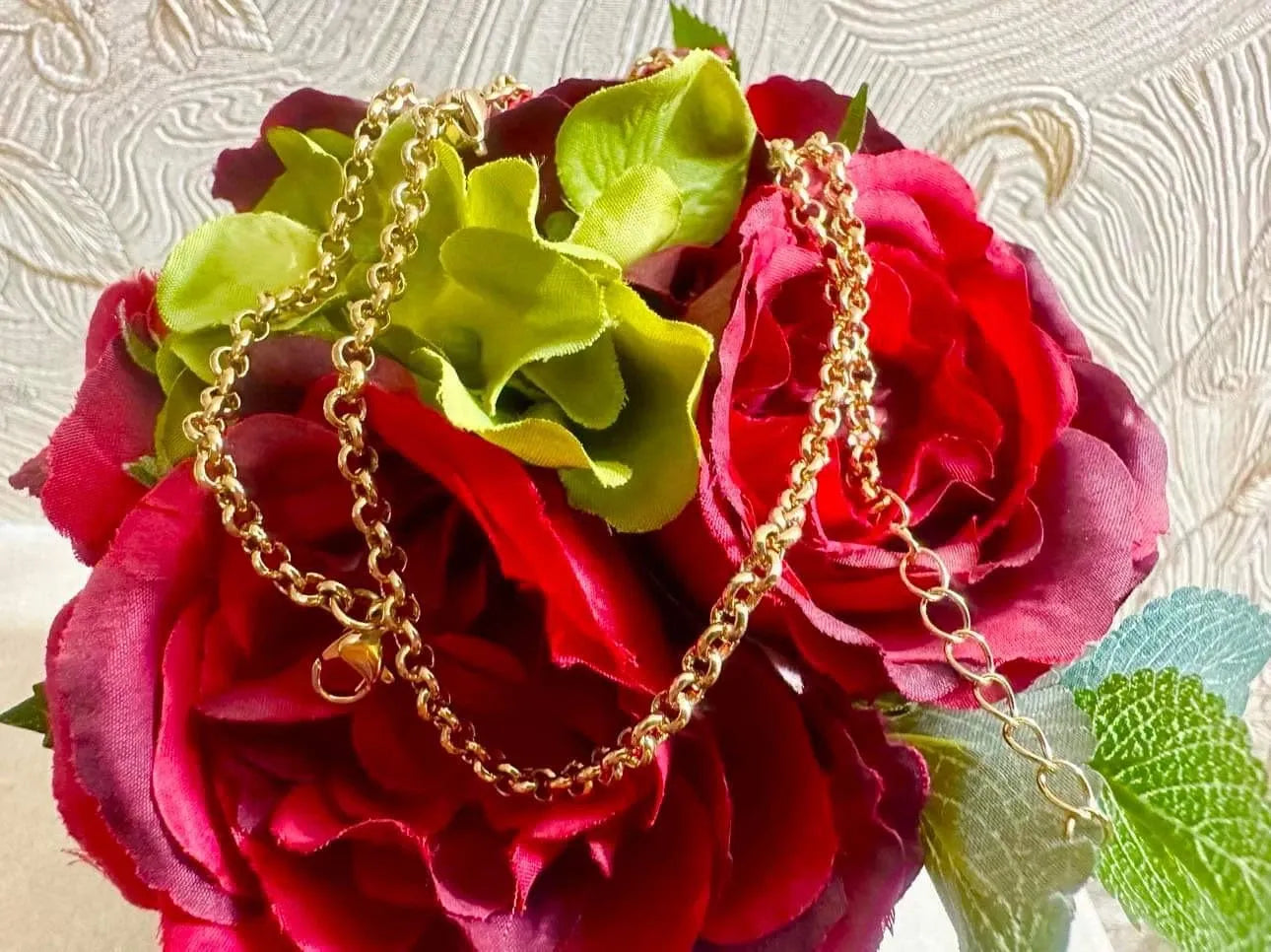 Gold chain necklace draped over red and green flowers on a textured background