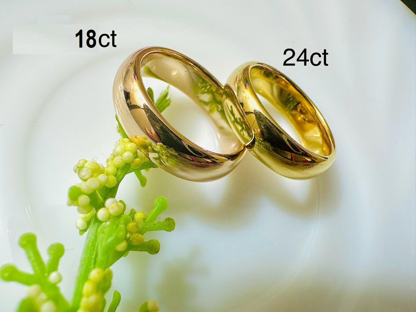 Two gold rings labeled '18ct' and '24ct' on a white background with greenery.