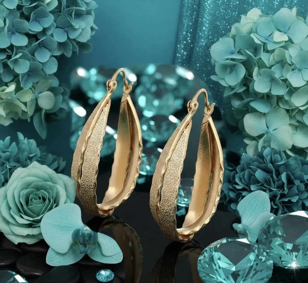 Gold hoop earrings with teal flowers and gemstones on a refl
ective surface