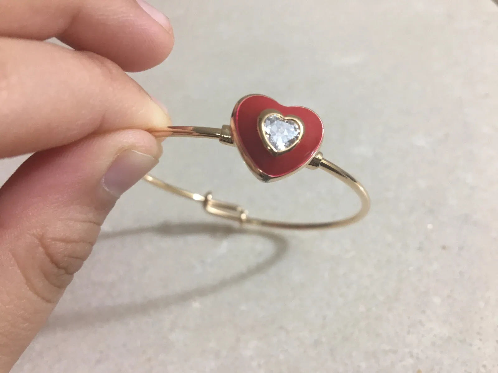 Red heart-shaped bracelet with a gold band held by a hand on a light background