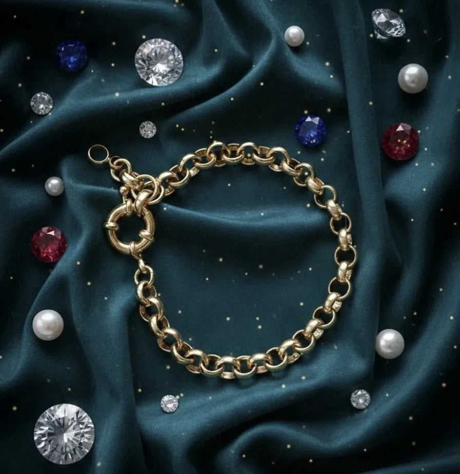 Gold chain bracelet on a dark blue fabric background with scattered gemstones.