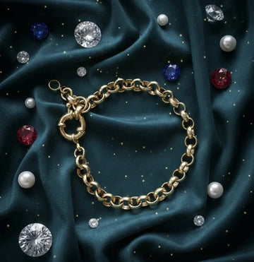 Gold chain bracelet on a dark blue fabric background with scattered gemstones.