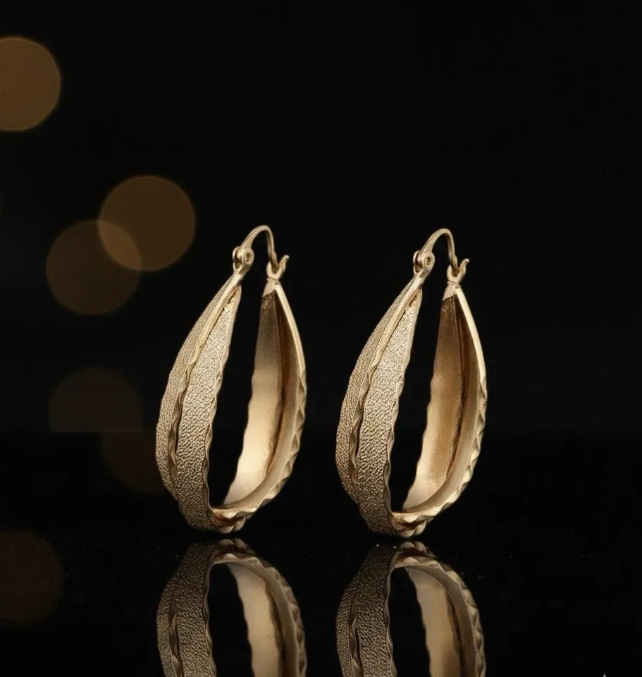 Gold hoop earrings on a reflective surface with a dark background