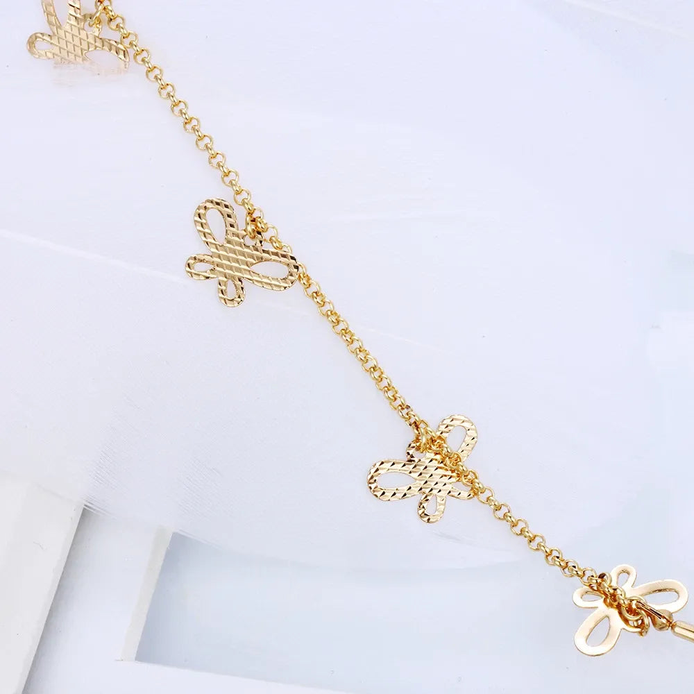 Gold chain bracelet with bow-shaped charms on a light gray background