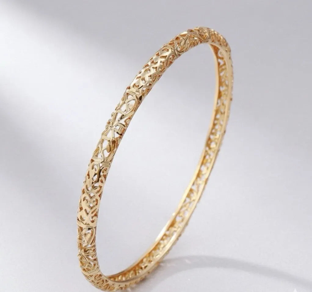 Gold bracelet with intricate design on a light gray background