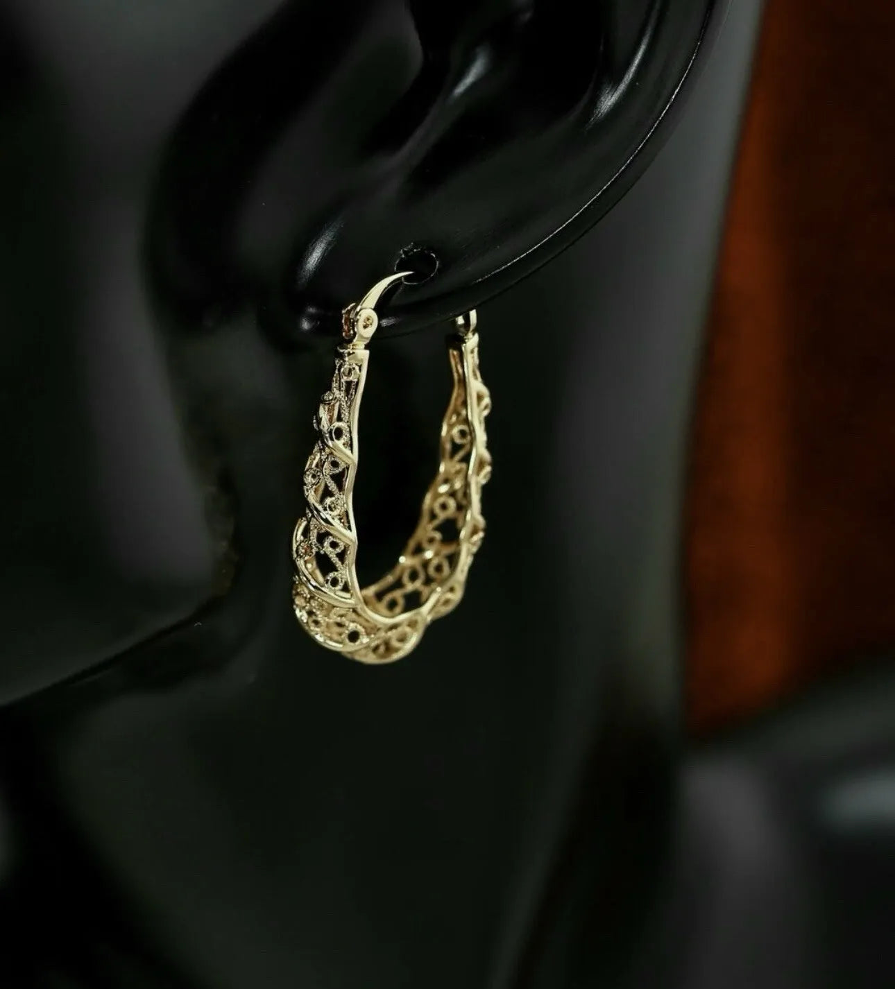 Gold hoop earrings on a black stand with a dark background