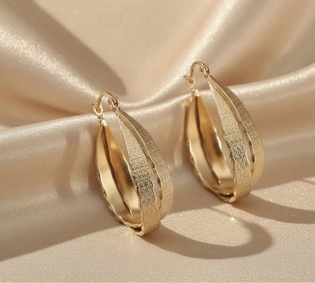 Gold hoop earrings with teal flowers and gemstones on a refl
ective surface