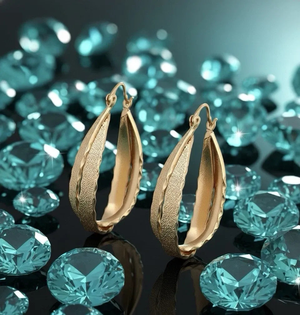 Gold hoop earrings with teal gemstones on a reflective surface