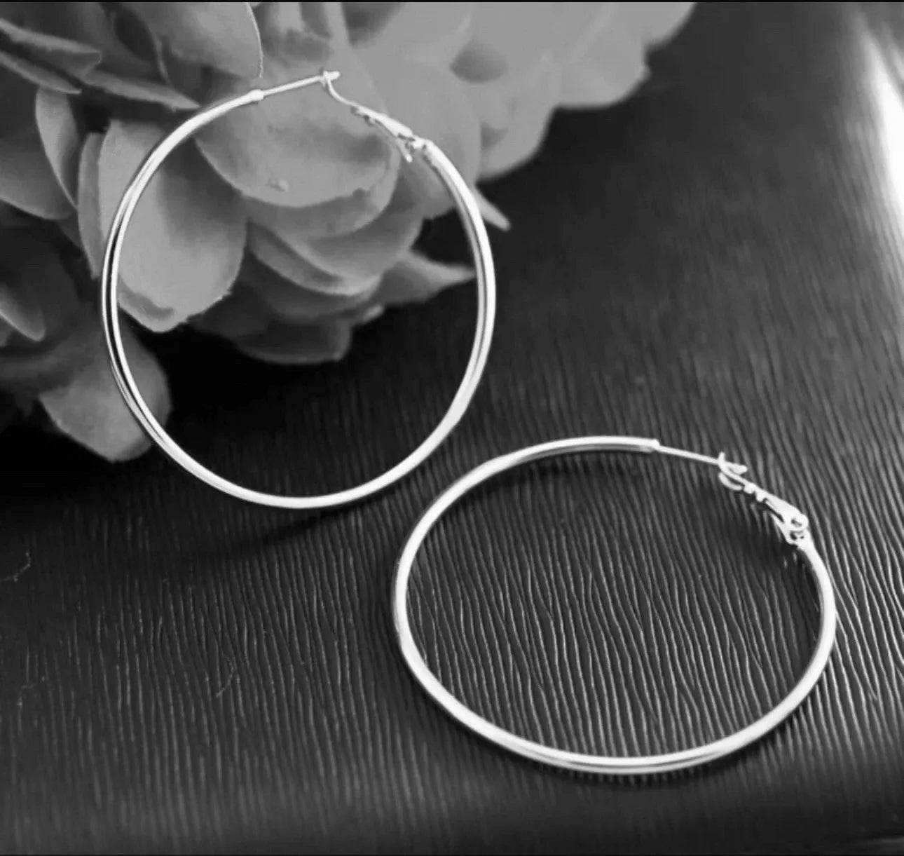 Two silver hoop earrings on a dark surface with flowers in the background