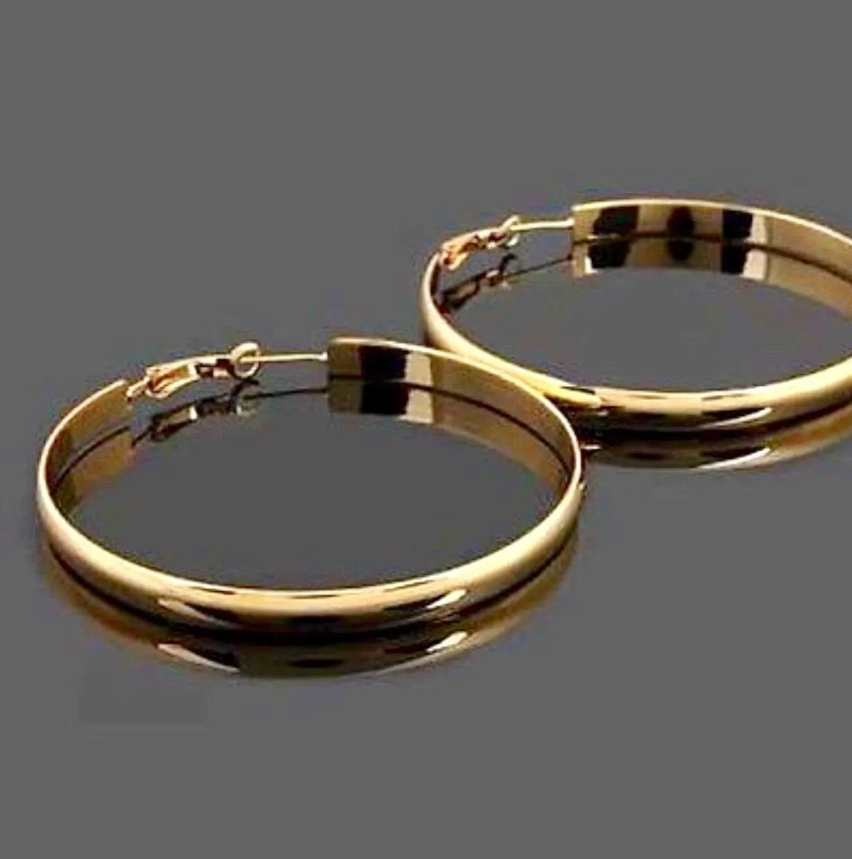 Gold hoop earrings on a reflective gray surface
