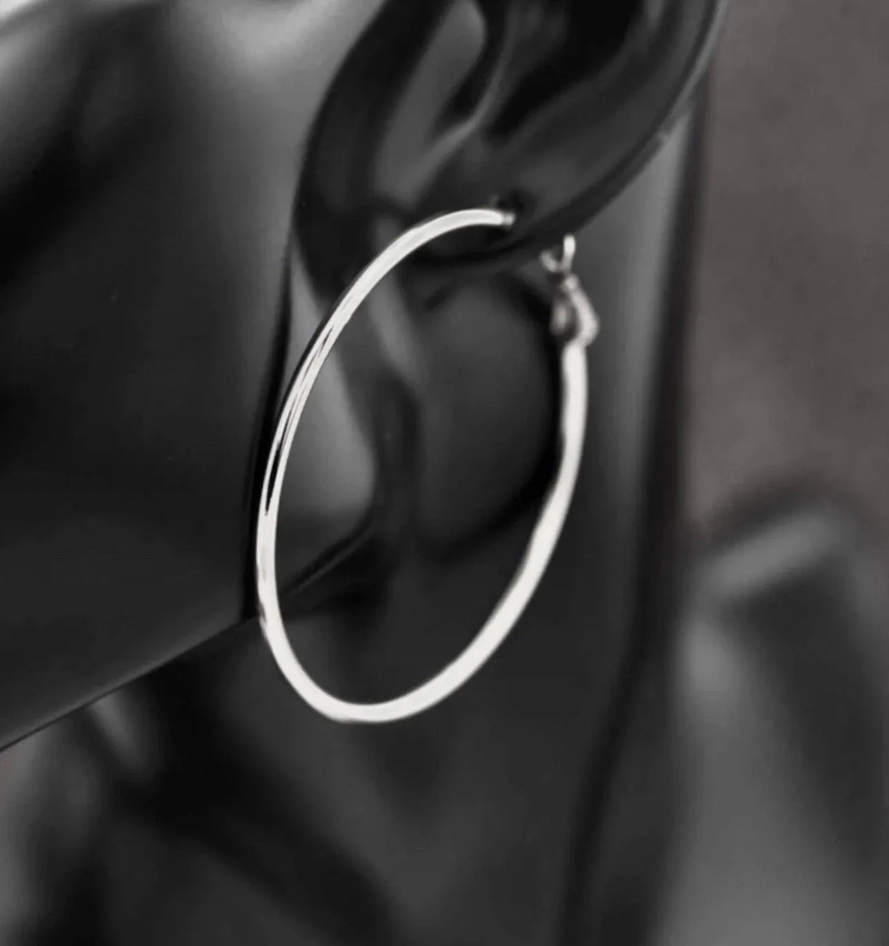 Silver hoop earring worn on an ear with a blurred background