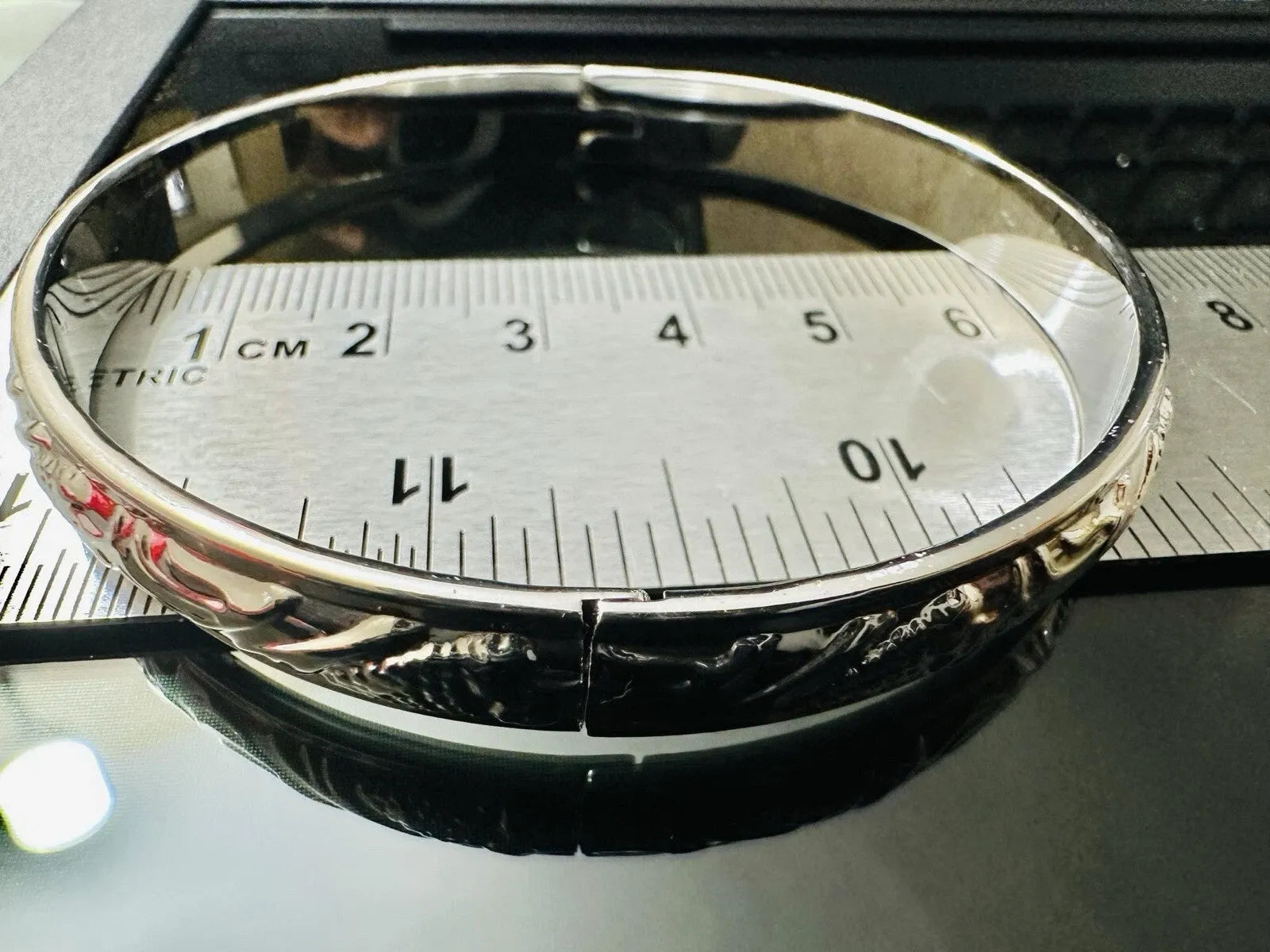 Silver bracelet with intricate design on a metallic surface with measurement scale.