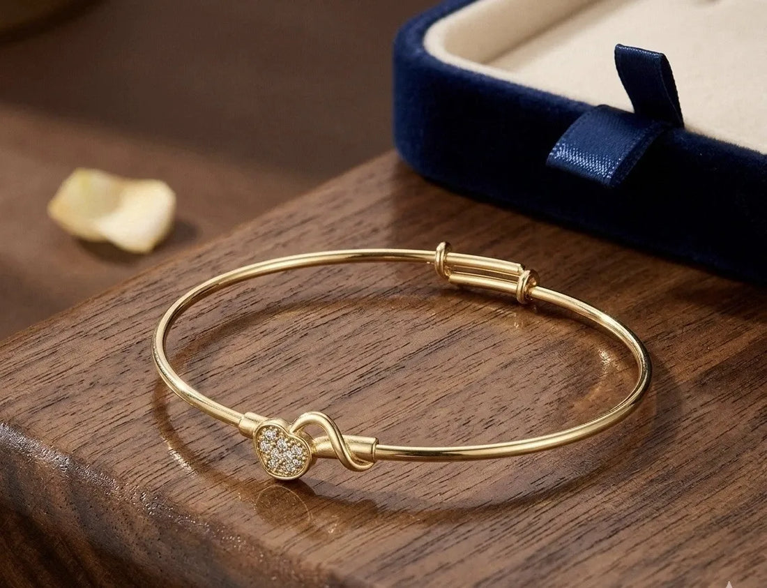 Gold bracelet with a heart-shaped clasp on a wrist against a neutral background