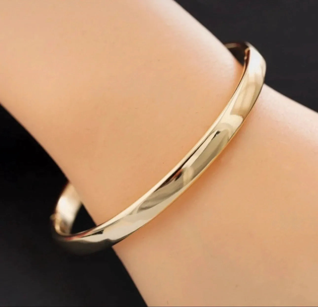 Gold bracelet on a wrist against a dark background