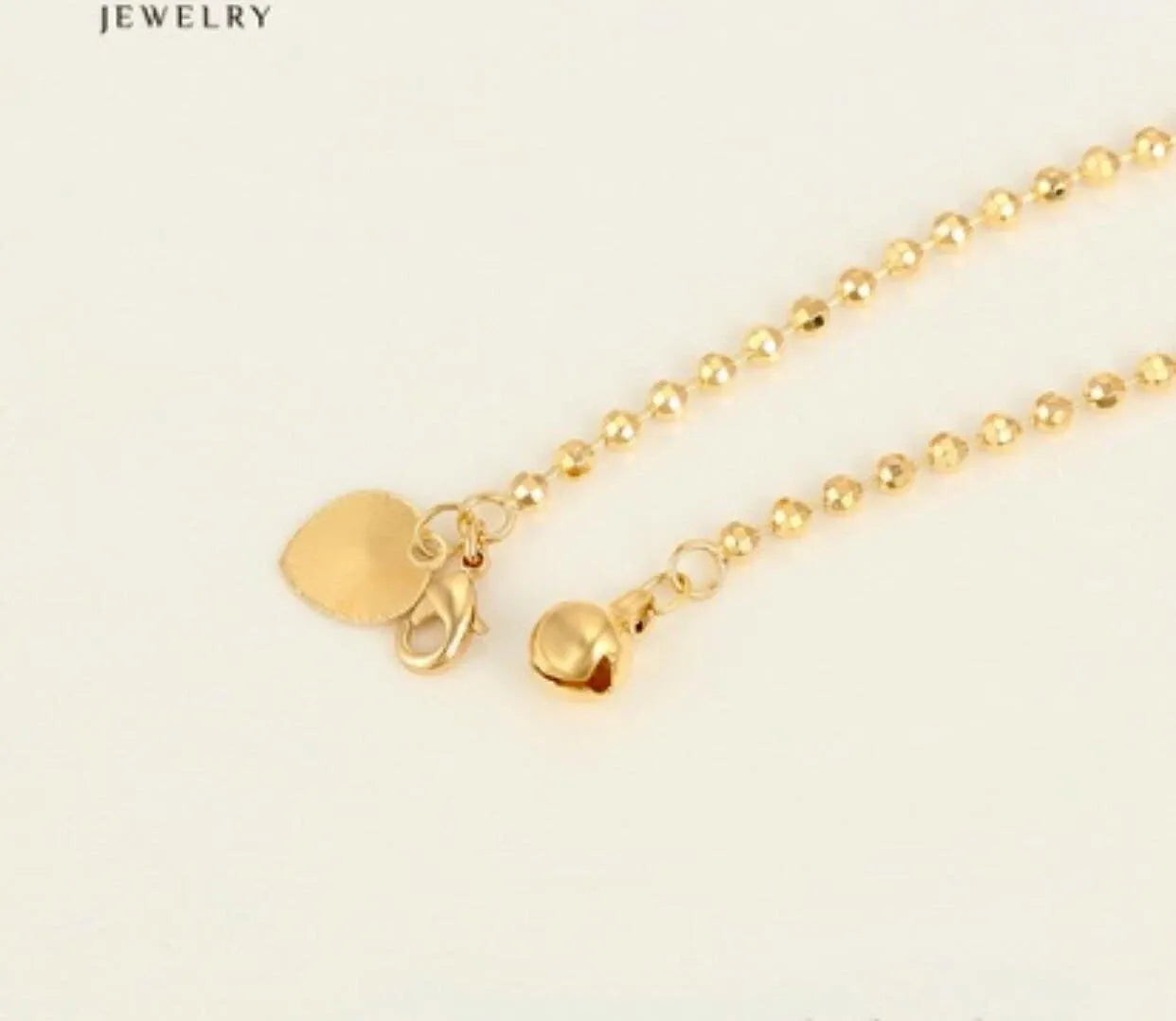 Gold bracelet with heart charm on a light beige background