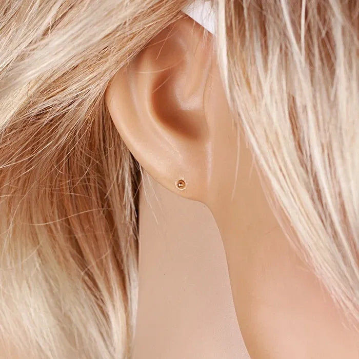Close-up of an ear wearing a gold earring with blonde hair.