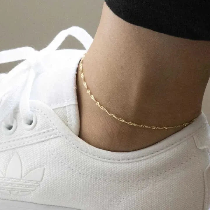 Gold anklet on a person's ankle with a white sneaker
