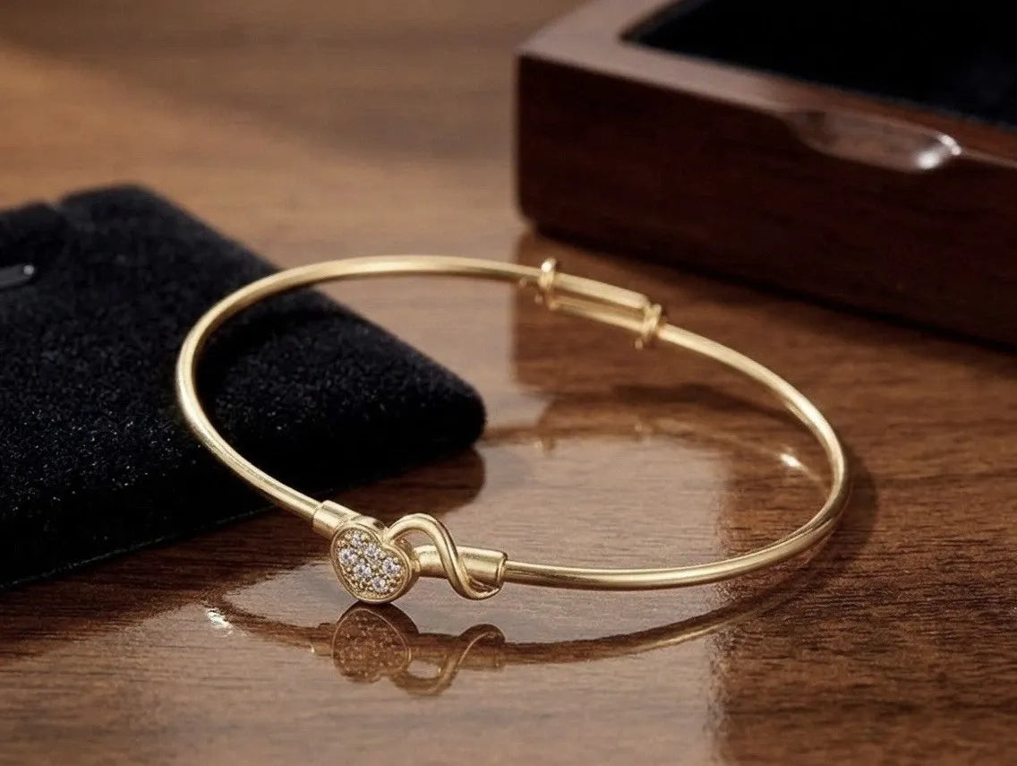Gold bracelet with a heart-shaped clasp on a wooden surface