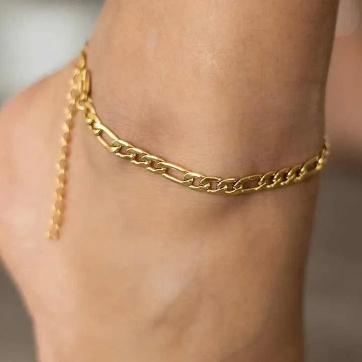 Gold chain anklet on a person's ankle against a neutral background