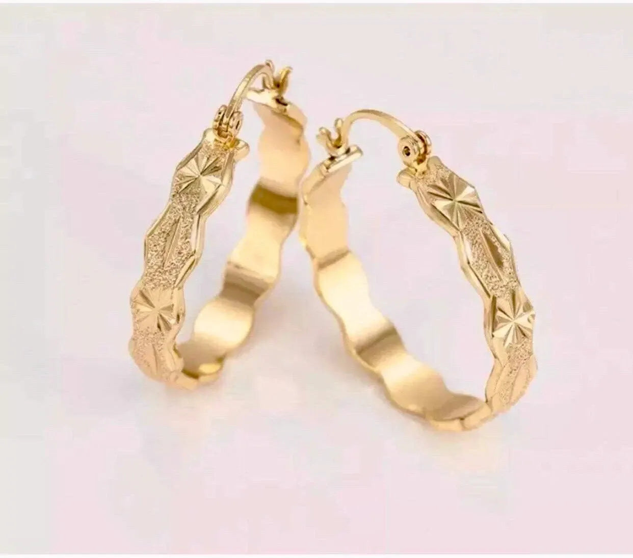 Gold hoop earrings with intricate designs on a light background