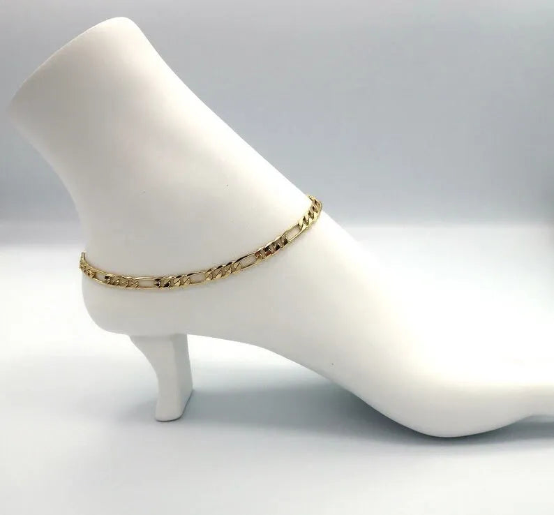 Beige sandal worn on a foot with a gold chain bracelet on a concrete floor.
