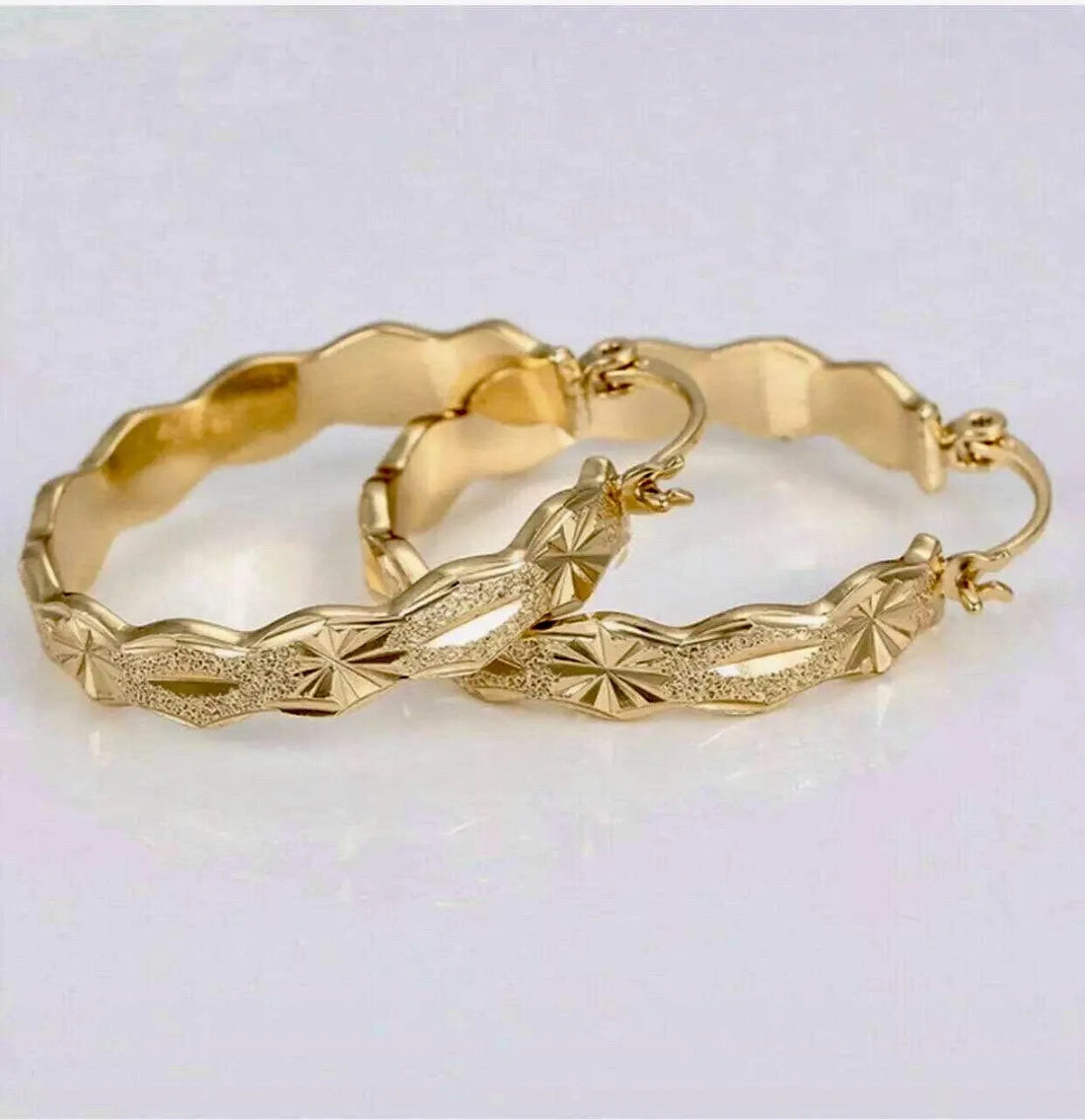 Gold hoop earrings with textured design on a light gray background