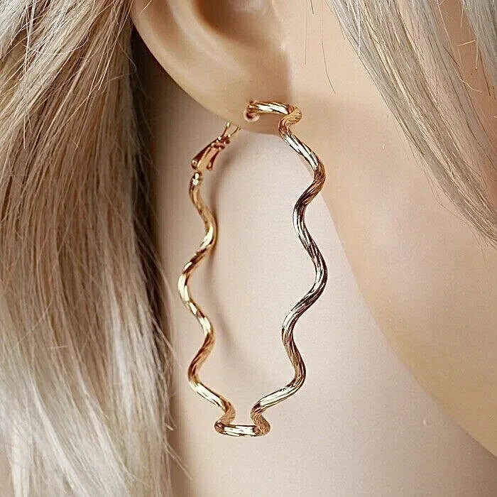 Gold spiral hoop earrings worn by a person with blonde hair.