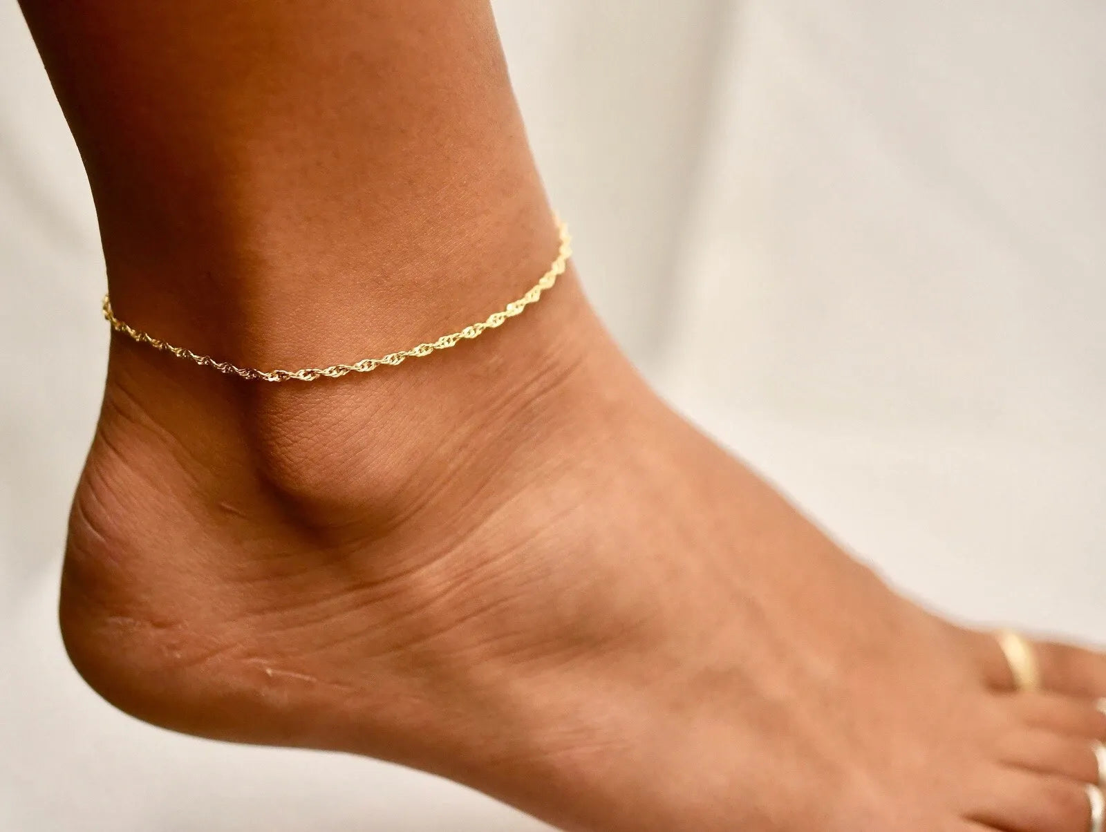 Gold anklet on a foot against a neutral background