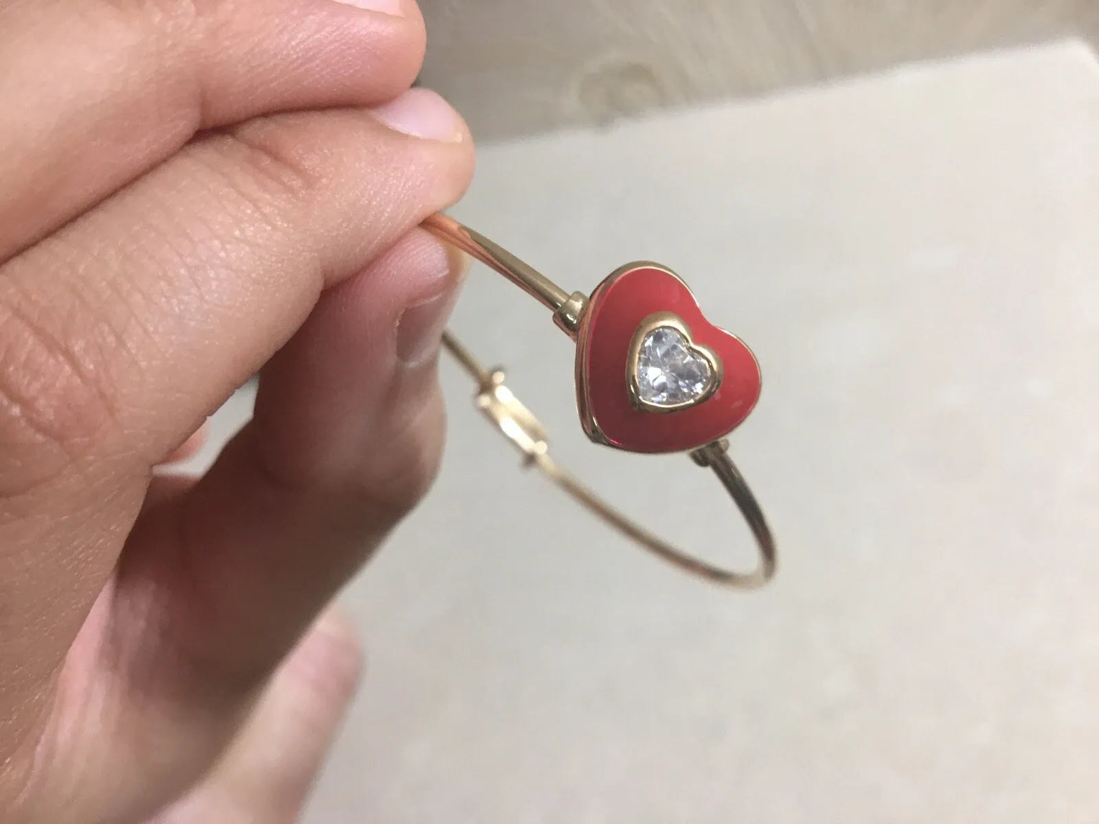 Hand holding a red heart-shaped bracelet with a clear gemstone on a light background