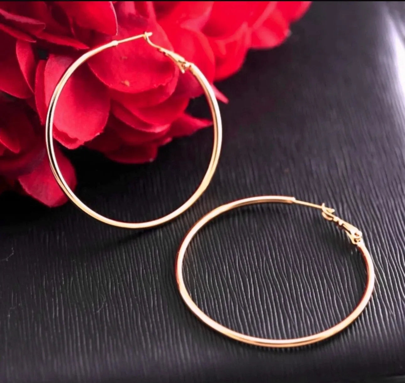 Gold hoop earrings on a dark surface with red flowers in the background