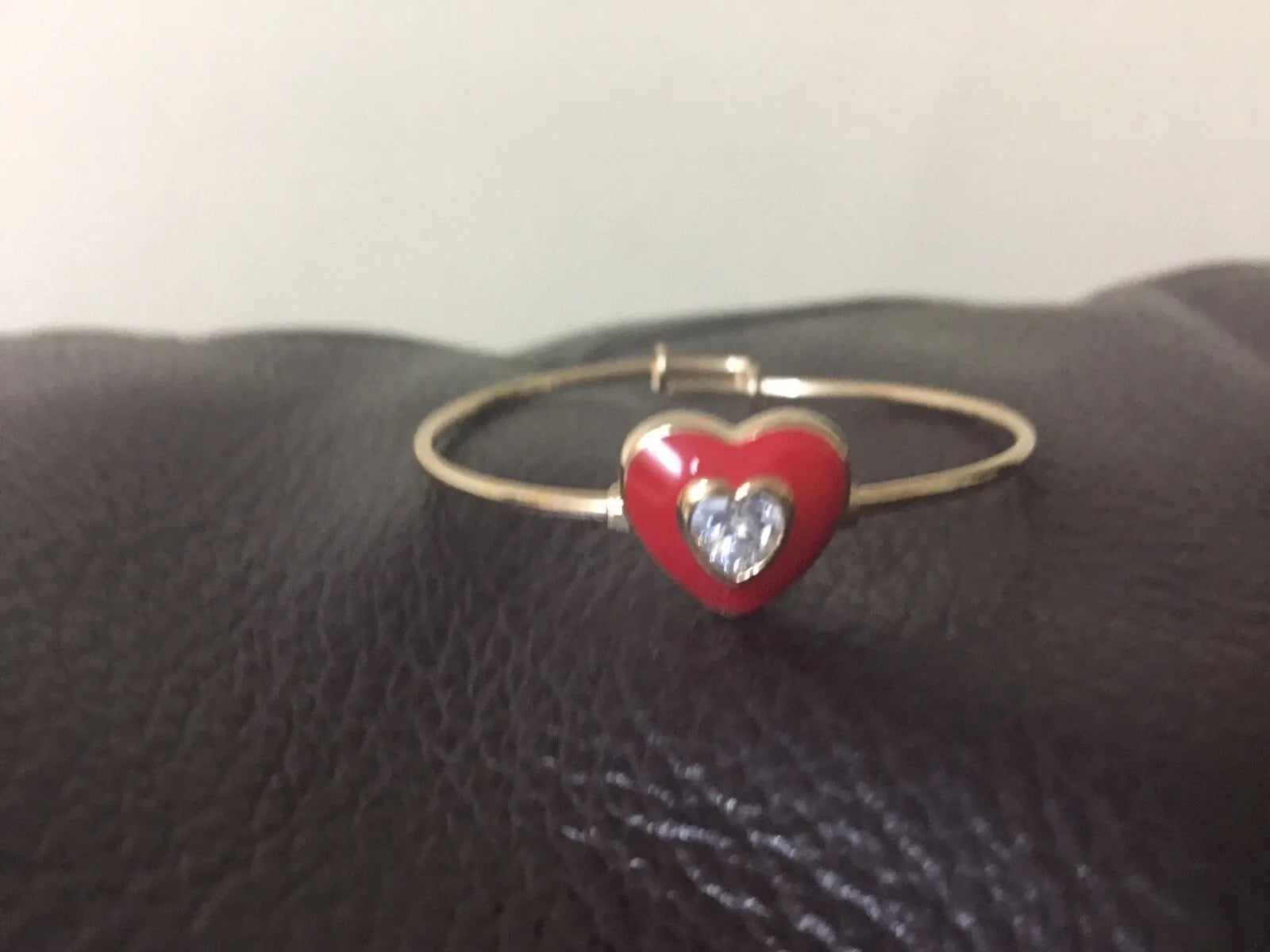 Gold bracelet with a red heart charm featuring a clear gemstone on a dark surface.