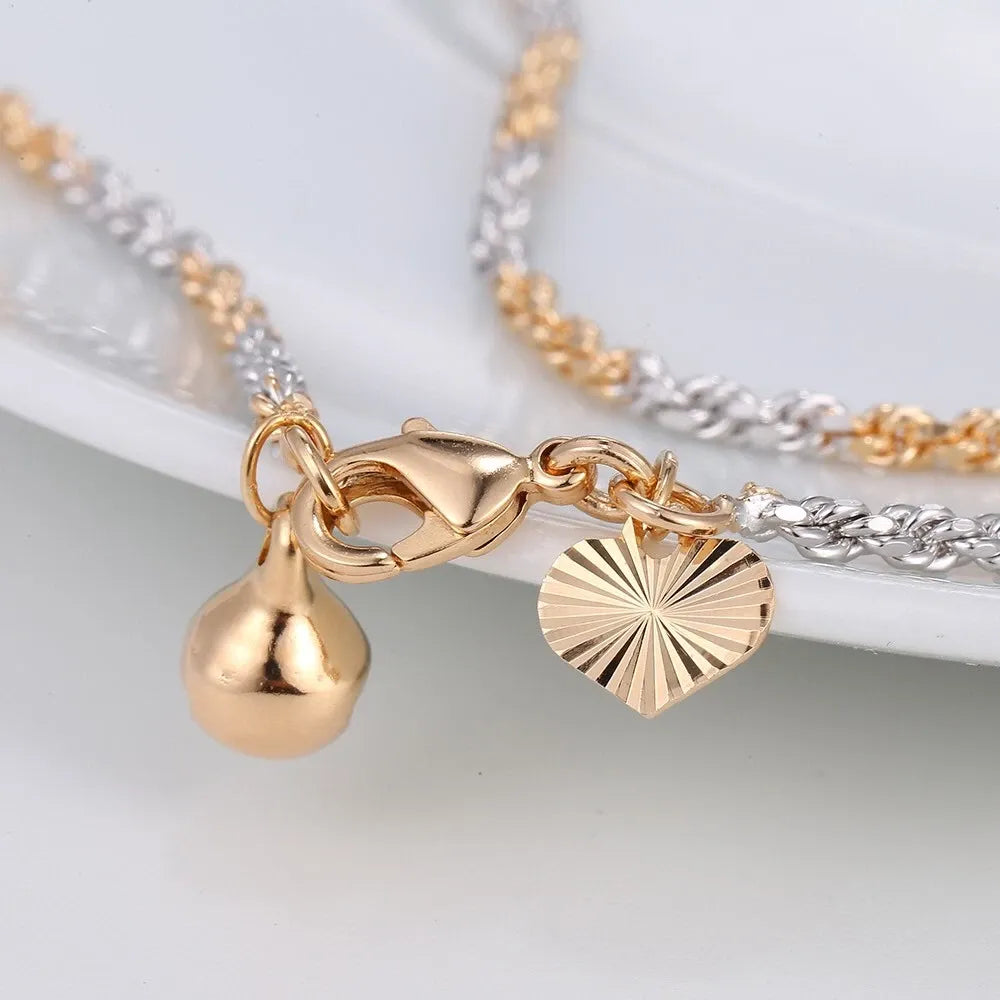 Close-up of gold and silver anklet with charms on a white background