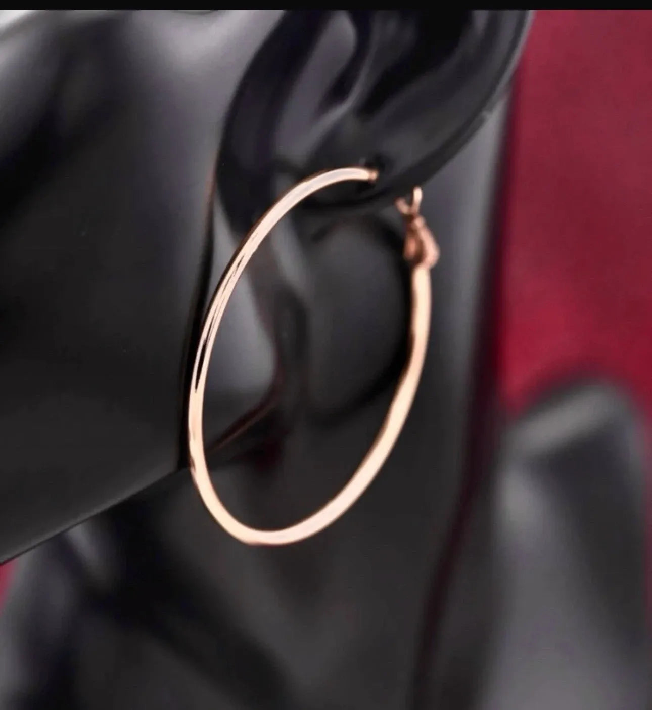 Rose gold hoop earring on a black stand with a blurred background