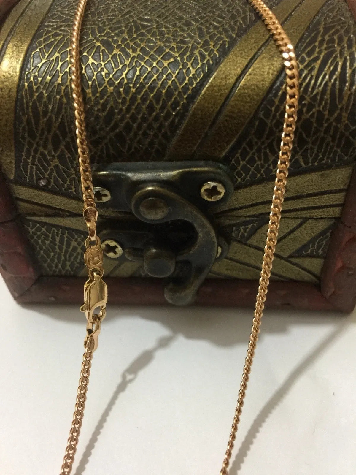 Gold chain with a clasp in front of an ornate, textured box.