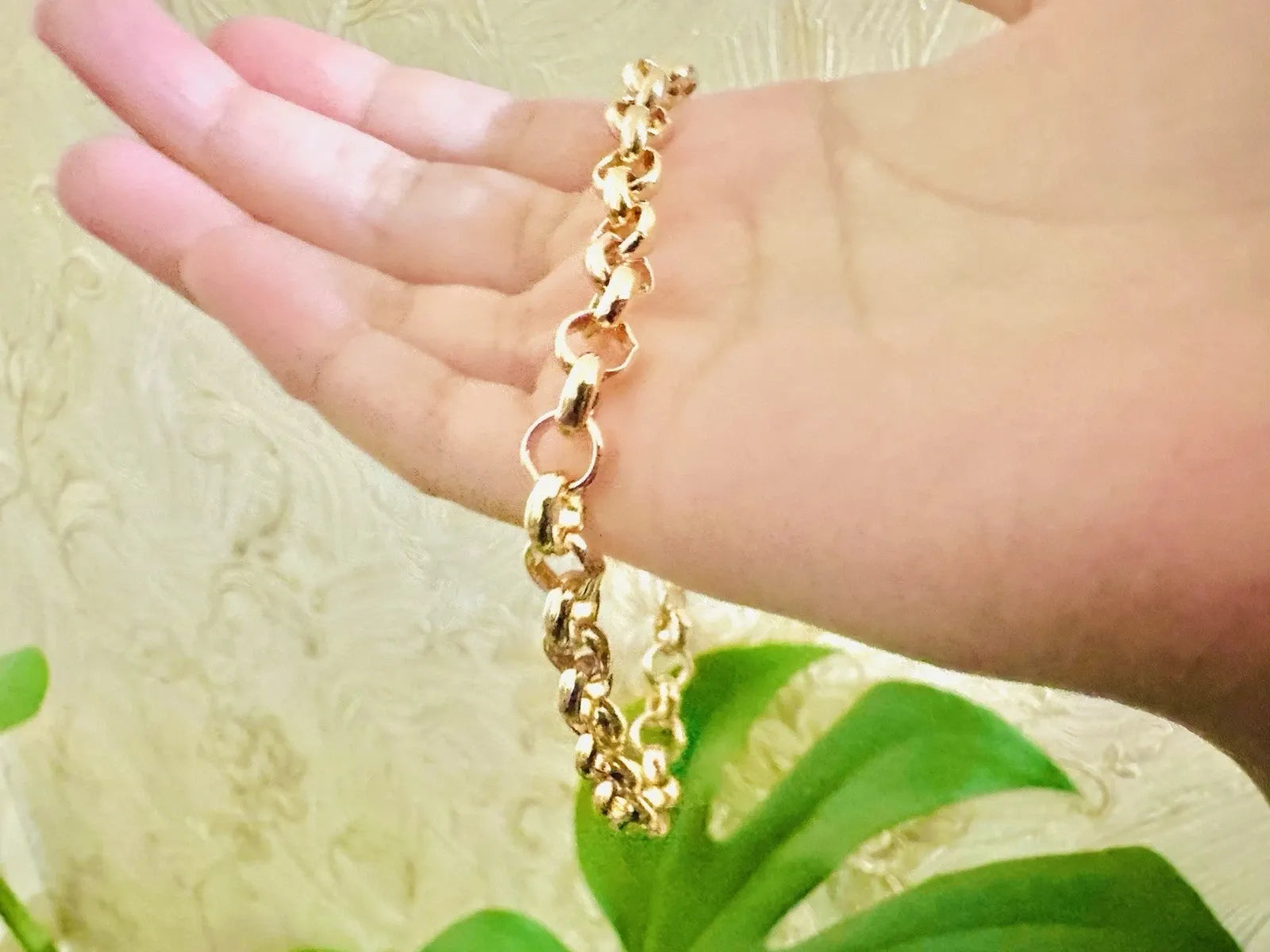 Gold chain bracelet on a hand with a blurred green plant background